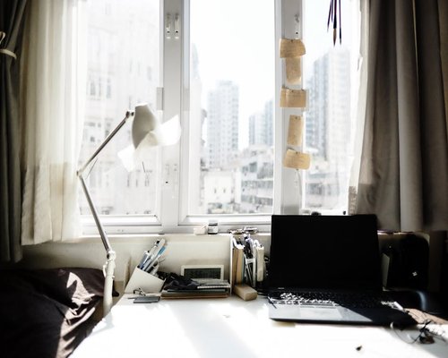 A beautifully organized working desk situated next to a large window filtering soft clean natural daylight